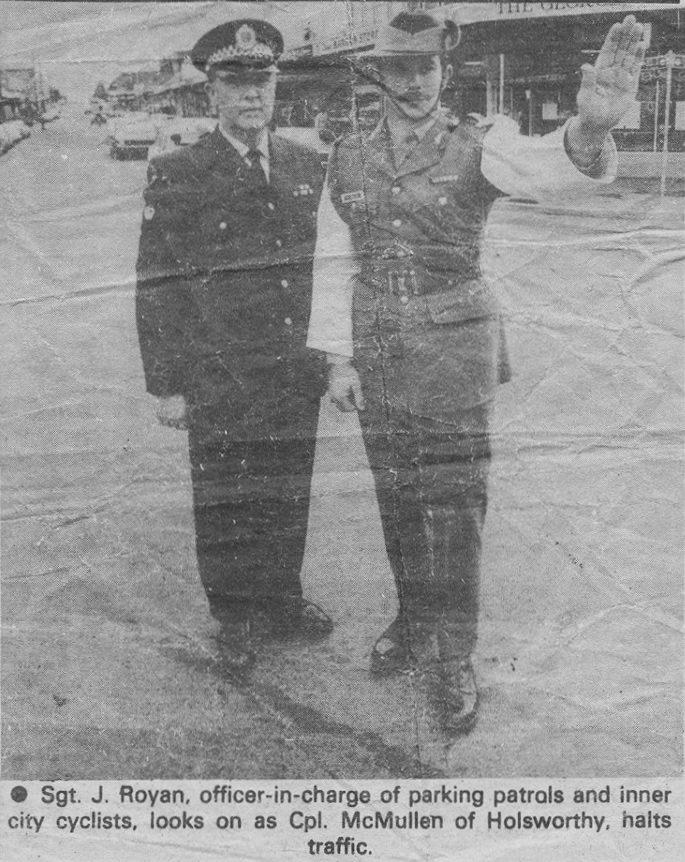 Sgt J. Royan, officer-in-charge of parking patrols and inner city cyclist, looks on as Cpl. McMullen of Holsworthy, halts traffic.